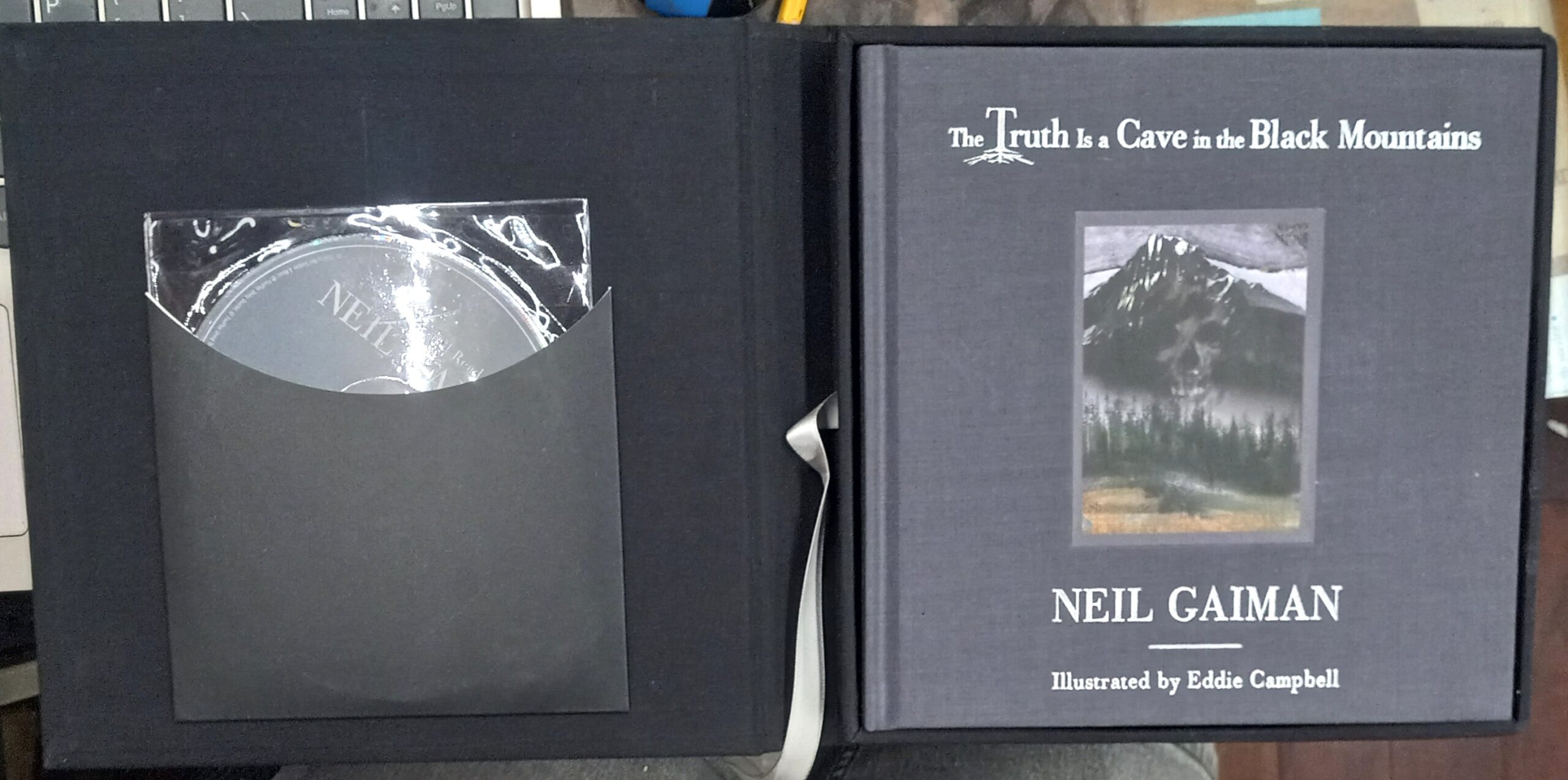 The Truth is a Cave in the Black Mountains open clamshell case with disc in pocket on one side and book with front board on the other